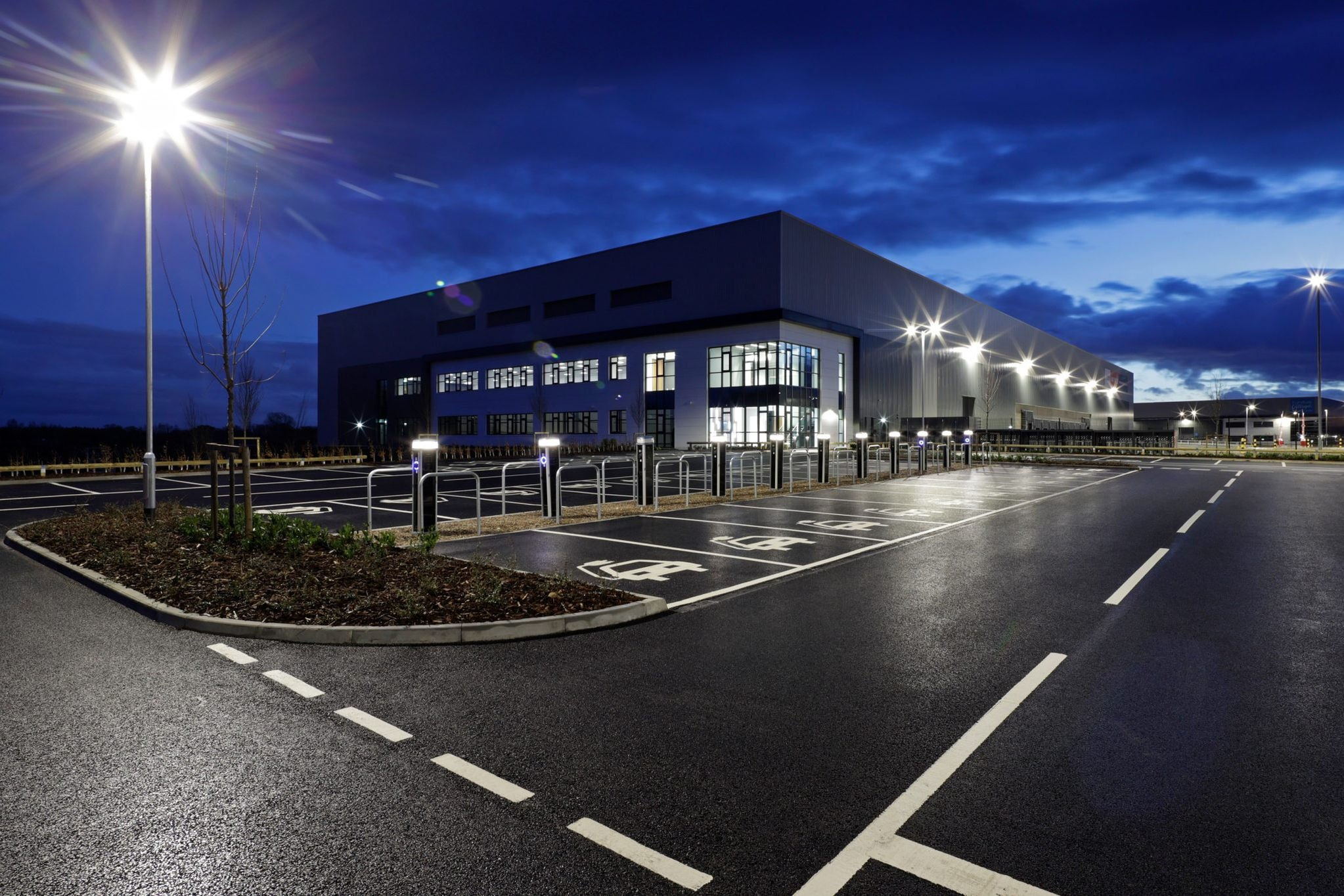 Lit EV charging bays outside a large commercial building at dusk